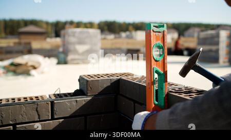 Mason ensuring level of a newly built brick wall using a spirit level during construction work on a sunny day Stock Photo