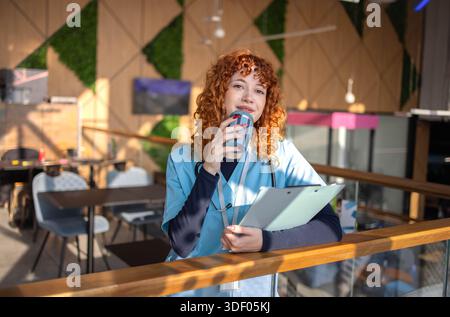 Mid adult female nurse taking a break in the hospital cafeteria, using a phone while enjoying a moment of relaxation Stock Photo