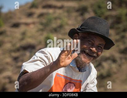 Smiling Malagasy Man with a beard waviing as he passes on a bicycle (not in view), Madagascar Stock Photo