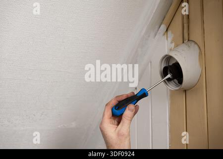 Hand using screwdriver to install or repair a ceiling light fixture. Stock Photo