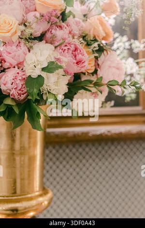Bright flowers in shades of pink and orange are arranged in a tall vase with a framed artwork behind them. Stock Photo