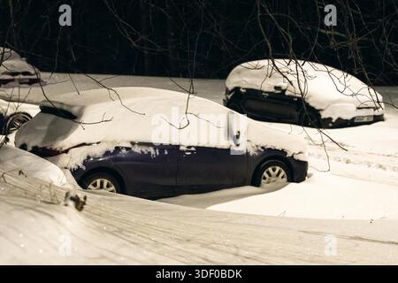Parked cars is completely covered in fresh snow after a heavy winter snowfall during a quiet nighttime scene Stock Photo