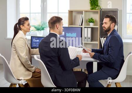 Colleagues reviewing finance analytics on screens during strategy meeting Stock Photo