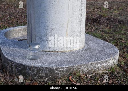A jar is sitting on the ground next to a cement pillar. The jar is empty and the pillar is dirty Stock Photo