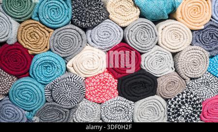 Tightly rolled fabrics in various patterns and colors stacked together, showcasing textile variety and rich textures. Stock Photo