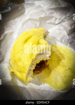 Partially eaten steamed yellow bao  bun with sweet or savory filling placed on crumpled white paper, malaysia Stock Photo