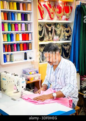 asian Man focused on stitching pink fabric using a sewing machine in colourful shop filled with threads and traditional jewelry singapore asia Stock Photo