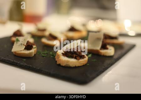A black tray with a variety of bread and cheese on it. The bread is cut into small pieces and the cheese is spread on top. The tray is placed on a whi Stock Photo