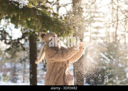 Smiling woman throws snow up. Happy young female plays with snow in sunny winter day. throw snow Stock Photo