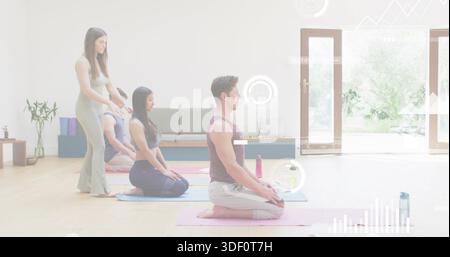 Practicing adults kneeling in bright studio in activewear, instructor adjusting posture, yoga mats Stock Photo