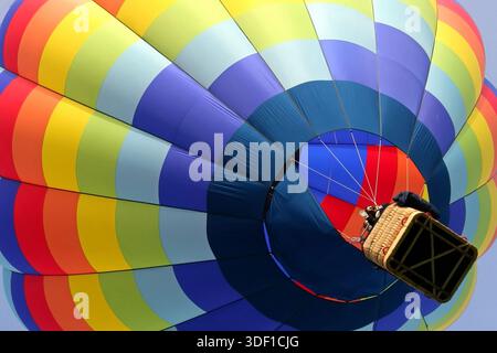 low angle view from inside a colorful hot air balloon looking up at the vibrant fabric panels and the wicker basket suspended above beatiful rainbow Stock Photo