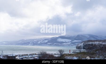 Winter sea and snow-covered mountains under cloudy skies in Otaru, Hokkaido, Japan. Stock Photo