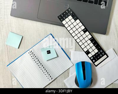 Workplace with laptop, blue wireless mouse, envelopes, notebook, office desk, sticky notes on a light wooden desk. Business, planning, remote work Stock Photo