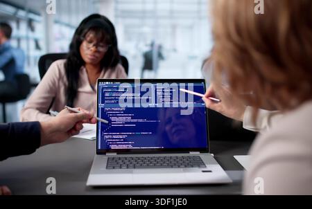 Team Of Engineers Developing Software In Busy Office Environment. Two Programmers Coding Together On Laptop Stock Photo