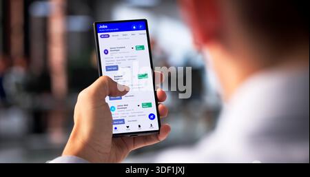 Young Hispanic Man Uses Smartphone To Search And Apply For Jobs. Stock Photo