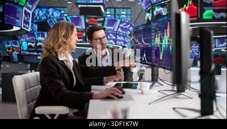 Man And Woman Trading Stocks On Computer At Stock Exchange. Possible Professions: Stock Broker, Analyst, Trader Stock Photo