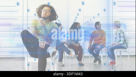 Sitting curly-haired man wearing glasses and sneakers in bright meeting room, showing blue overlay Stock Photo