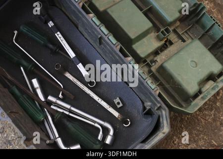 Old open green plastic toolbox filled with rusted metal wrench and dirty mechanic tool set for manual repair work on dusty ground showing heavy indust Stock Photo
