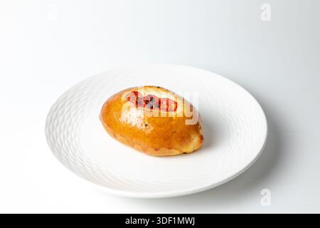 Close-up of bun with roasted tomato filling, appetizing baked good on white background. Stock Photo