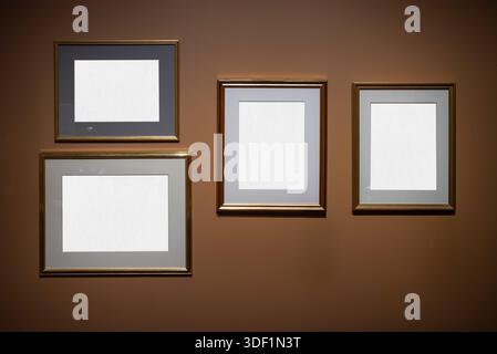 Four rectangular frames with gold edges hang on a brown wall. Each frame has a white mat with space for text or images. Stock Photo