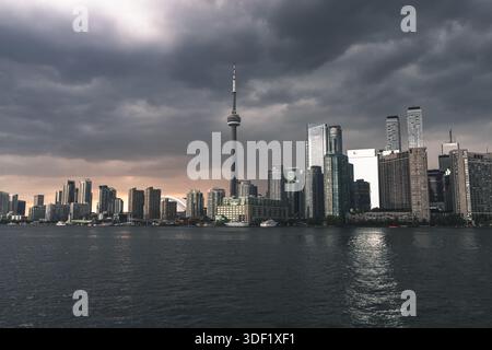 View of Toronto's skyline, a mix of modern skyscrapers and the iconic CN Tower, reflecting in the dark waters under a dramatic, stormy sky, Toronto, O Stock Photo