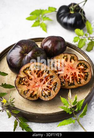 Sliced "Marsha’s Starfighter Beefsteak" tomatoes (Solanum lycopersicum) on a ceramic plate with leaves and stems. Rare heirloom tomato suitable Stock Photo