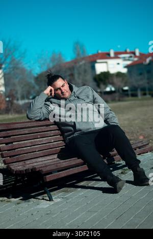 Man resting head on hand, sitting on a park bench, enjoying urban outdoor lifestyle Stock Photo