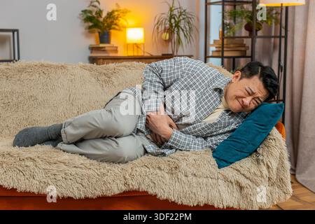 Mature ill sick man lying on couch feeling sudden strong abdominal stomach ache, gastritis problem. Middle-aged guy having symptom poisoning diarrhea indigestion peptic ulcer pancreatitis at home. Stock Photo