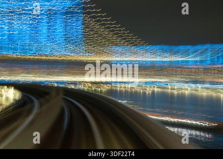 View of blurred lights streak across the night sky above the curving tracks in a mesmerizing display of urban movement, Tokyo, Tokyo, Japan. Stock Photo
