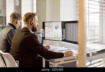 Call center analysts with headsets monitoring data on multiple computer screens Stock Photo