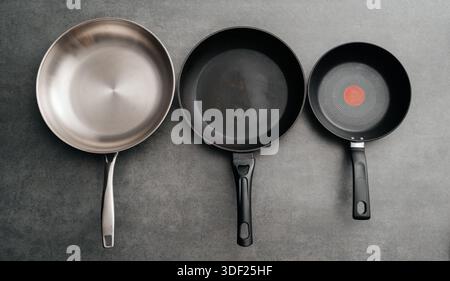 Trio of cookware with matching handles displayed together, Series of three stainless steel frying pans with distinct nonstick and speckled finishes Stock Photo