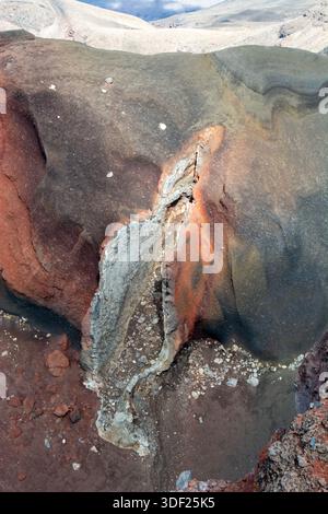 Aerial view of a colorful volcanic rock formation showcasing layers of red, gray, and brown earth. The texture is rough with visible cracks and minera Stock Photo