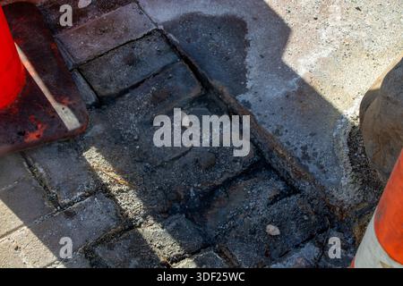 A close-up view of a construction site showing uneven brick pavement with gravel and debris. Traffic cones are partially visible, indicating ongoing w Stock Photo