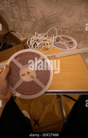 Person's hand grasping a white spool of red LED lights with other cables and reels on wooden desk Stock Photo