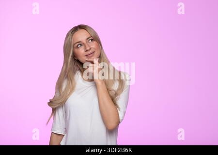 Thoughtful young woman thinking, smiling, pondering, considering what to choose and looking up Stock Photo
