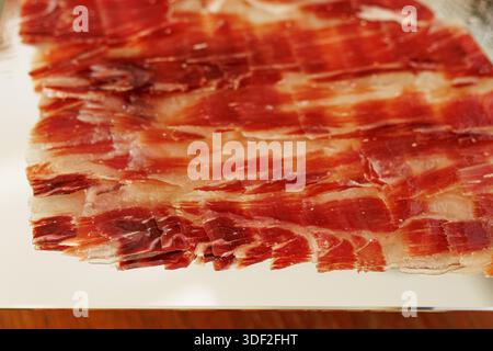 Close-up of thinly sliced cured ham arranged in overlapping layers on a reflective tray. Stock Photo