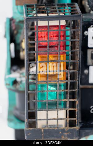 Machine mounted signal indicator featuring red yellow and green lights enclosed in metal safety cage used for industrial equipment operation monitorin Stock Photo