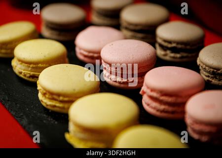 Selection of pastel macarons arranged on a dark slate platter. Stock Photo