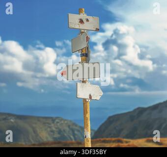 Several blank direction signs on wooden pole against dramatic blue sky and mountains, concept of choice, decision and uncertainty. Stock Photo