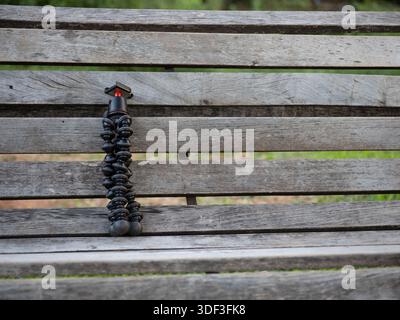 Flexible camera tripod positioned on a wooden bench in a park, representing mobile content creation and outdoor filming. Stock Photo