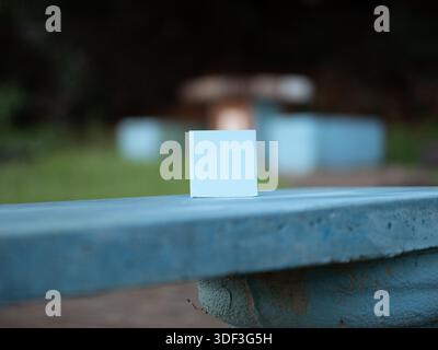 Blank white sticky note on a blue bench outdoors, shown as a minimalist reminder with copy space. Stock Photo