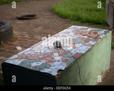 Wired computer mouse on a mosaic bench outdoors, suggesting an improvised workspace in a public park. Stock Photo