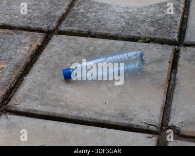 Empty plastic bottle on paving tiles outdoors, highlighting urban litter and environmental pollution. Stock Photo