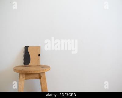 Kraft notebook on a wooden stool against a white wall, shown as a clean branding mockup with negative space. Stock Photo