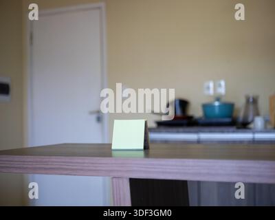 Folded sticky note on a wooden table with a blurred kitchen background, representing a home reminder and planning. Stock Photo