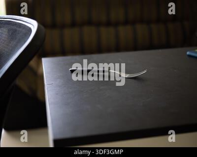 Single fork on a black table near a chair, representing an empty table concept and minimalist dining setup. Stock Photo