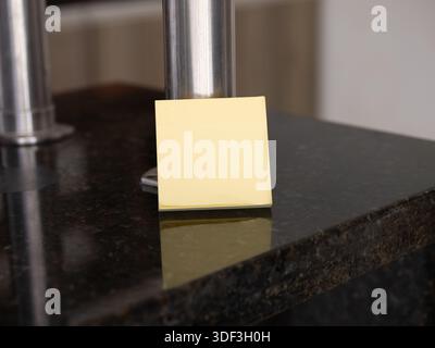 Yellow sticky note on a granite countertop near a metal stand, representing kitchen reminders and home planning. Stock Photo