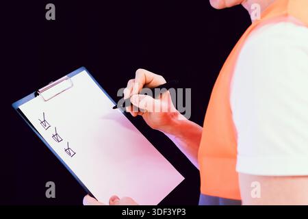 Construction worker in orange vest using pen to mark items on clipboard checklist. Stock Photo