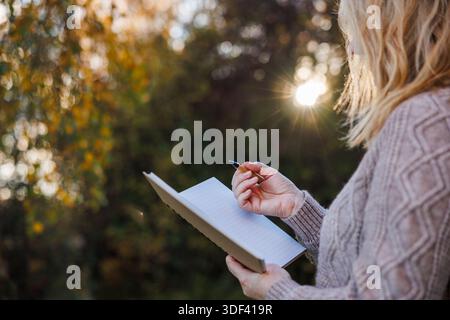 Woman writing notes to her diary during sunset in forest. Journaling and write inspiration for fresh start goals Stock Photo