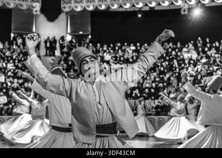 The Şeb-i Arus ceremony at the Mevlana Kültür Merkezi in Karatay, Konya, Turkey, a venue that can accommodate 3,000 people, shows dervishes during the ritual Sema dance. The right hand points upwards, receiving God's blessing. The left hand points downwards, passing it on to the earth. The dervishes turn anticlockwise, symbolically against the ego. The right foot stays fixed while the left foot drives the rotation. Şeb-i Arus is the annual festival marking the death anniversary (17 December) of the mystic poet Rumi (Jalāl ad-Dīn ar-Rūmī, 1207–1273), founder of the Mevlevi order, celebrated as  Stock Photo